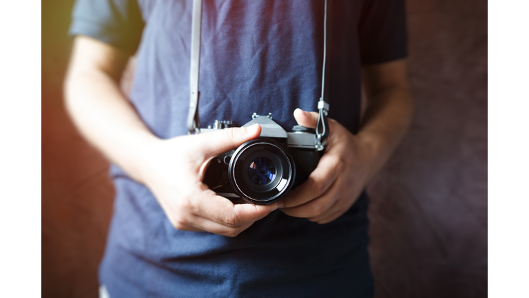 Midsection Of Man Holding Digital Camera Against Wall