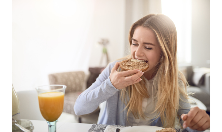 Close-Up Of Young Woman Eating Breakfast At Home
