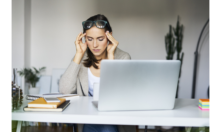 Young woman at home with laptop on desk touching her temples