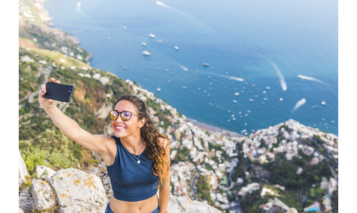A young woman is taking a selfie. Positano village in the background
