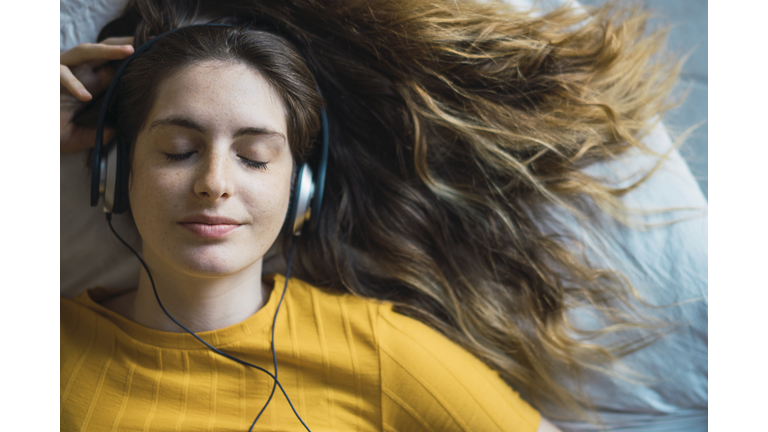 Portrait of smiling young woman lying on bed listening music with headphones