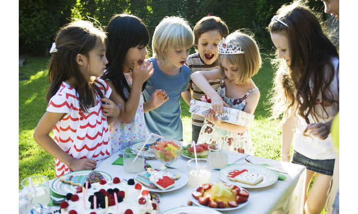 Girl opening gift at birthday party as friends watch