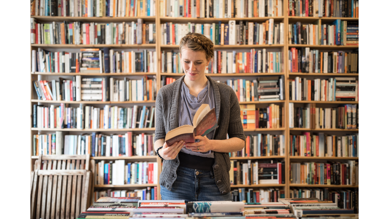 Beautiful young female customer reading book at bookstore