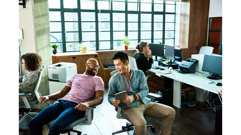 Two men chatting in office with digital tablet