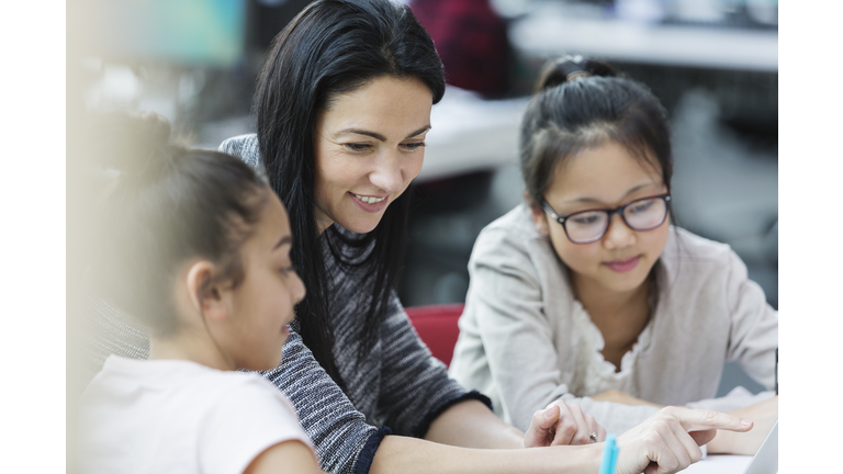 Female teacher and girl students using laptop in classroom