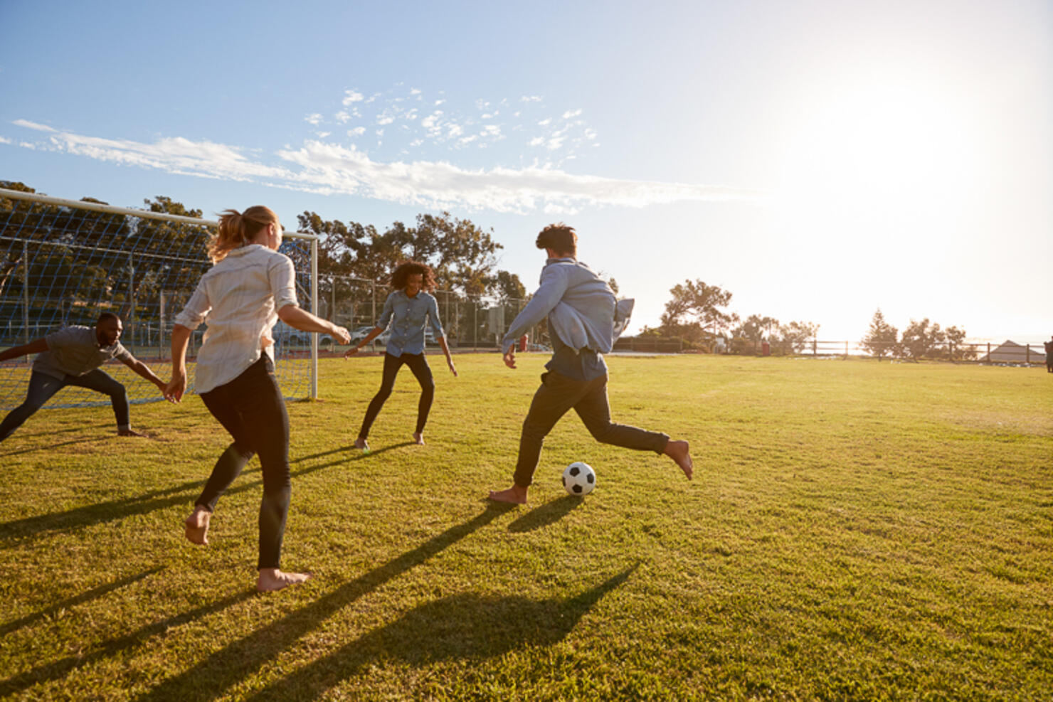 Four young adults playing football in a park at sunset