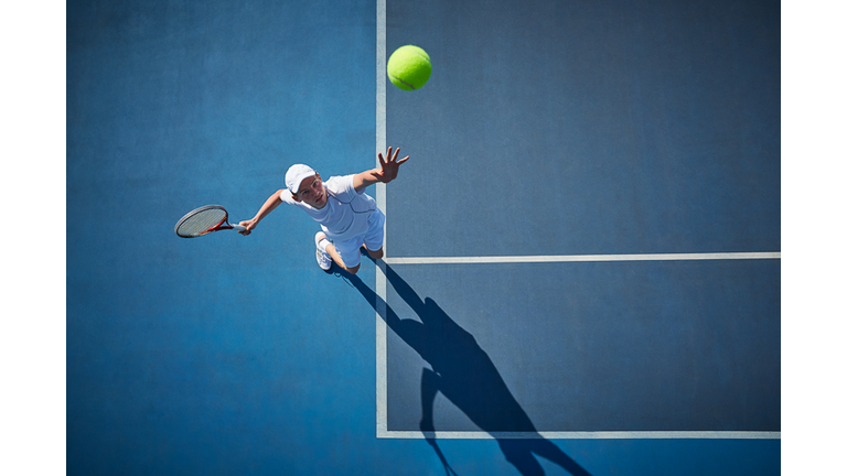 Overhead view of young male tennis player playing tennis, serving the ball on sunny blue tennis court