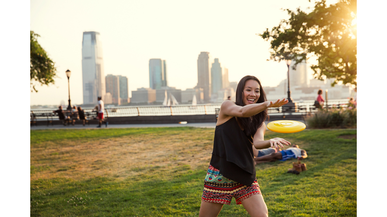Happy woman catching plastic disc while standing in park against clear sky