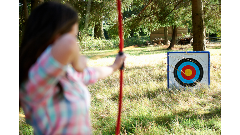 Rear view of teenage girl practicing archery with target