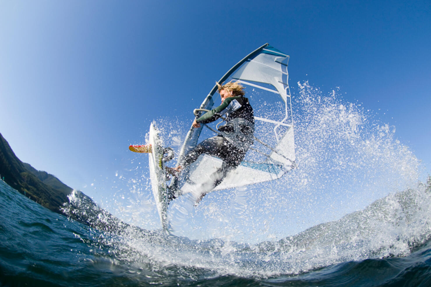 Man jumping wave on windsurf board, low angle view