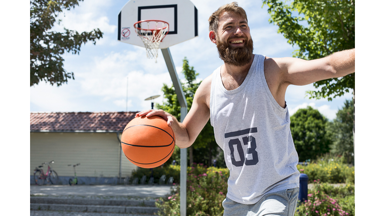 Laughing man playing basketball on outdoor court