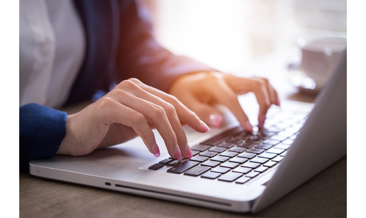 Close-up of hands typing on laptop keyboard in the office.