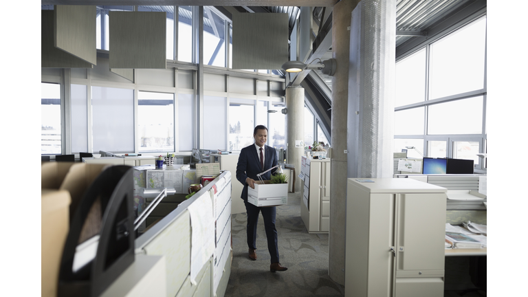 Businessman being laid off, carrying box of belongings in office