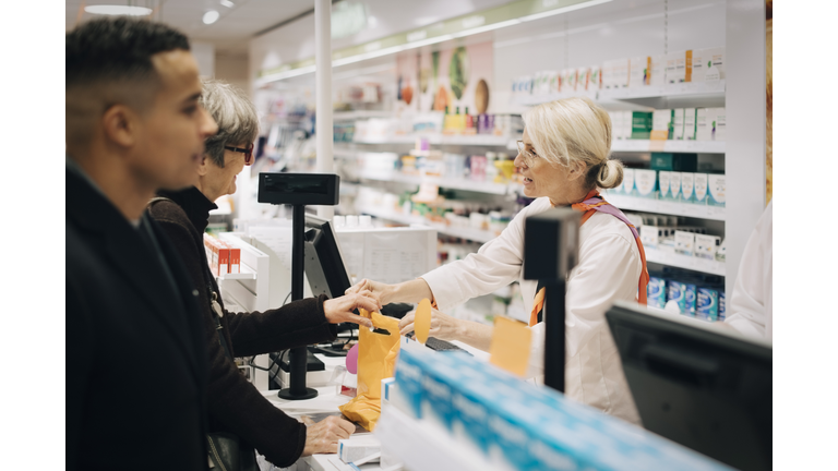 Pharmacists and customers standing at checkout in medical store