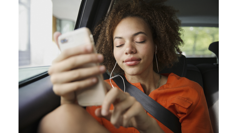 Serene young woman listening to music with headphones and mp3 player in back seat of car