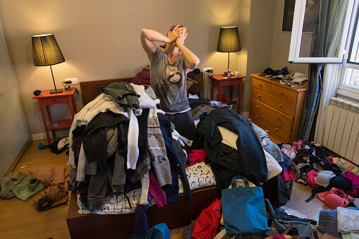 Portrait of woman crying among tiles of clothes in a messy bedroom