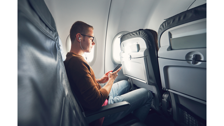 Man Listening Music While Using Mobile Phone In Airplane