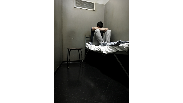 Male Prisoner Sitting On Bed In Prison