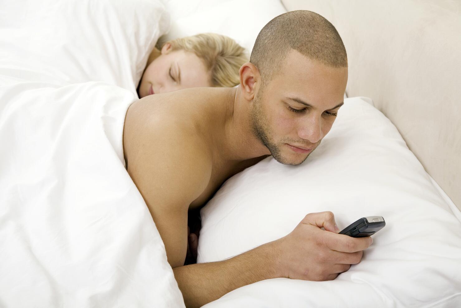 Young man text messaging with young woman sleeping