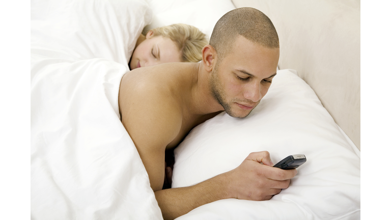 Young man text messaging with young woman sleeping