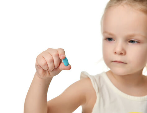 Young baby girl hold light blue headache  pill medicine tablet in small hand