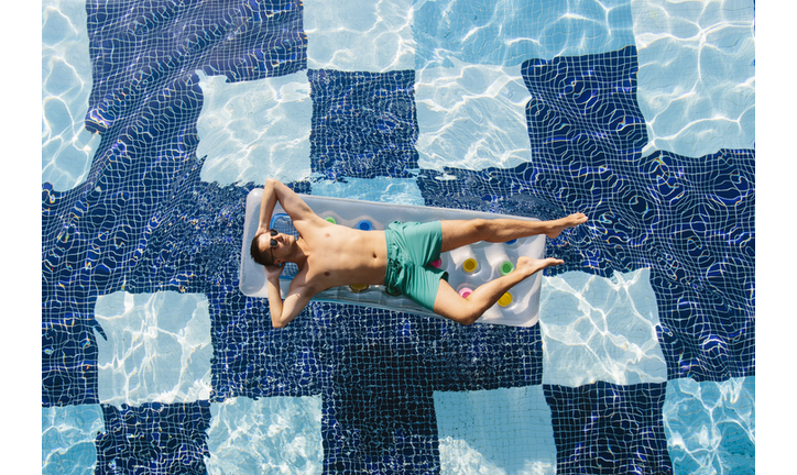 High angle view of a young man in sunglasses sunbathing in swimming pool on inflatable pool raft