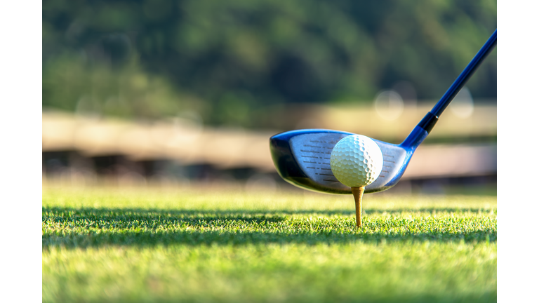 Close up golf ball and driver, player doing golf swing tee off on the green sunset evening time, presumably does exercise.  Healthy and Lifestyle Concept.