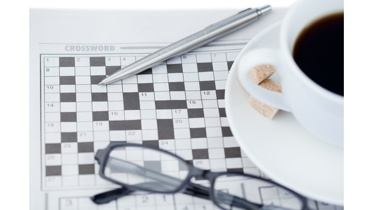 A cup of coffee a pen a pair of glasses and a crossword puzzle