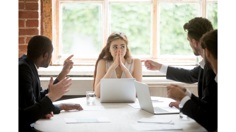 Perplexed young woman looking at coworkers pointing fingers at her.