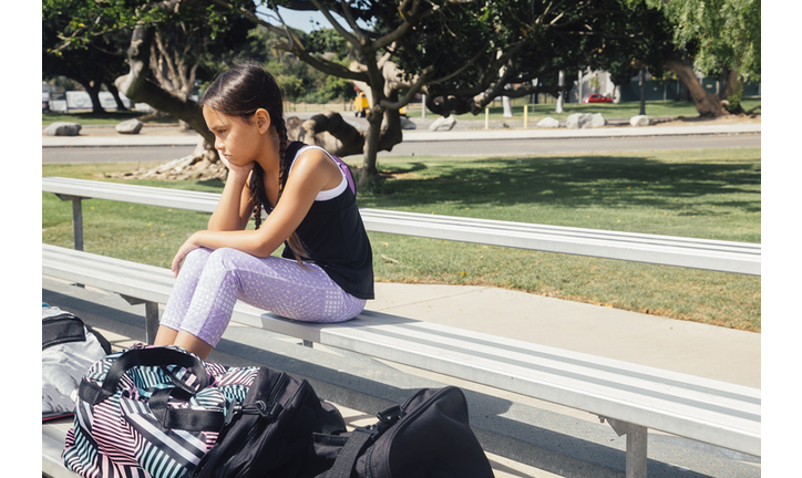 Schoolgirl soccer player alone on bench on school sports field
