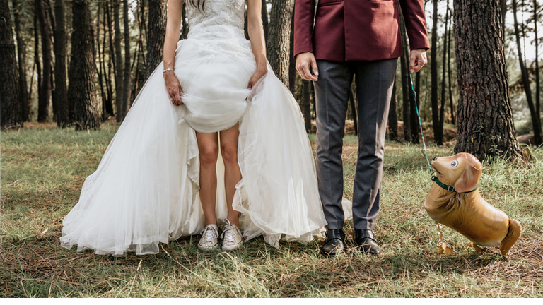 Low section of bride and groom in forest with funny dog-shaped balloon