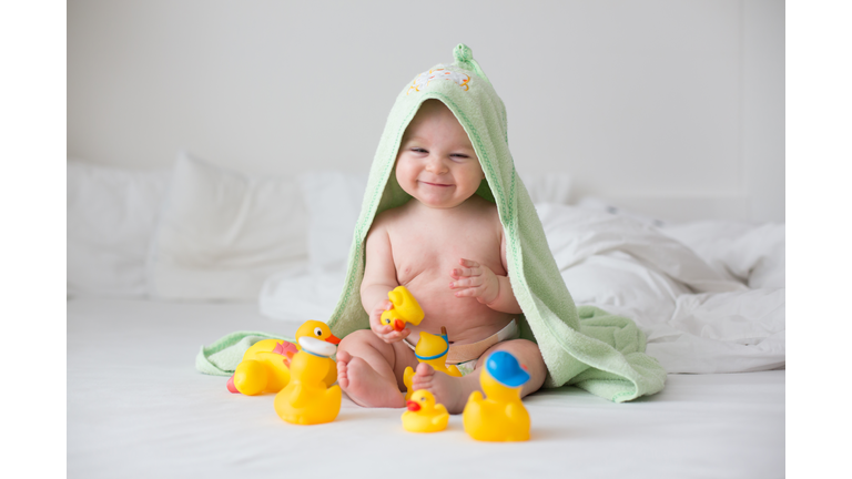 Cute little baby toddler boy, playing with rubber ducks after bath in bed
