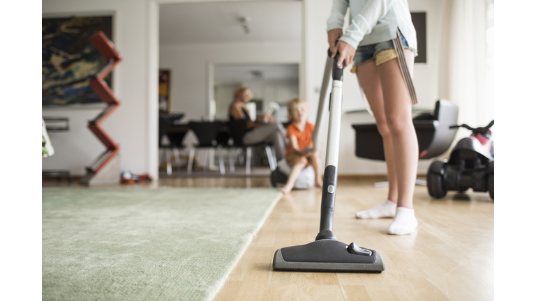 Low section of girl cleaning floor with vacuum cleaner at home