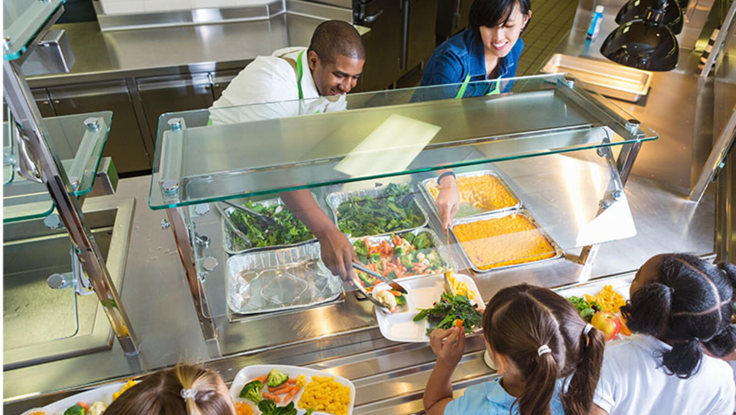 Cafeteria worker serving trays of healthy food to children