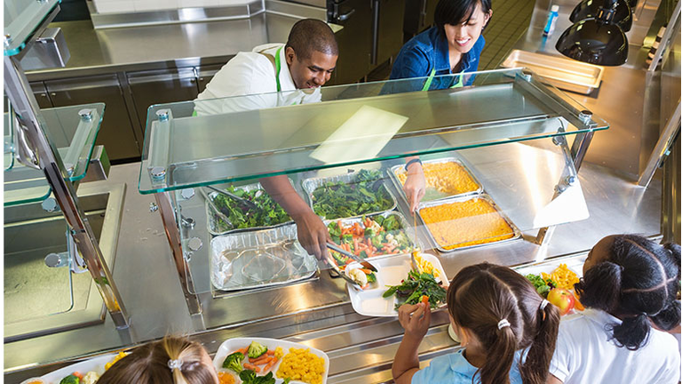 Cafeteria worker serving trays of healthy food to children