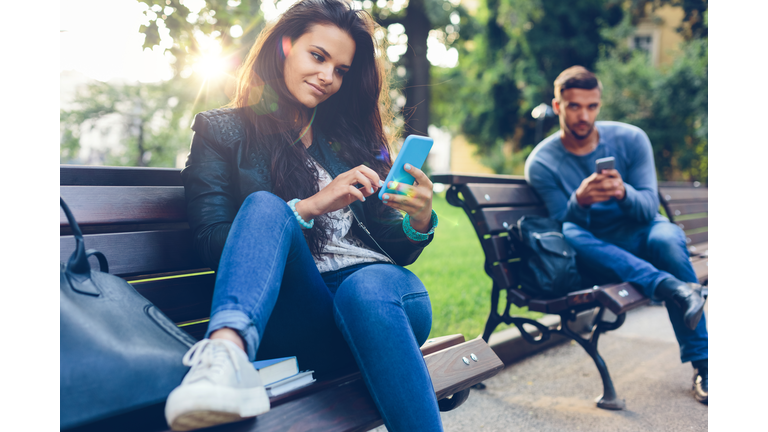 Young couple in the park texting on smartphones getty images