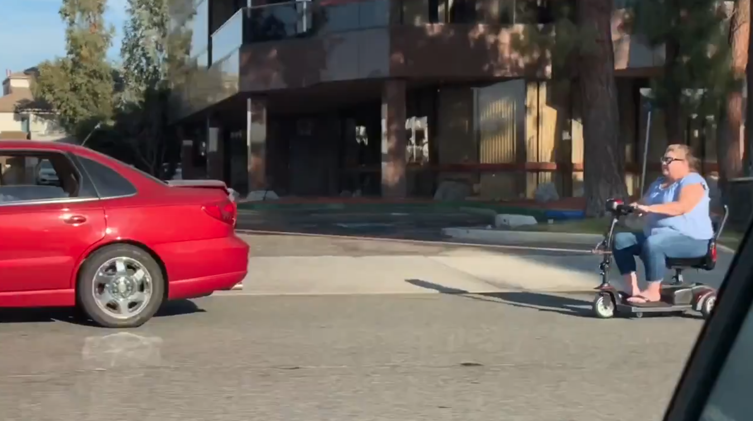 Woman on mobility scooter seen being towed by red sedan