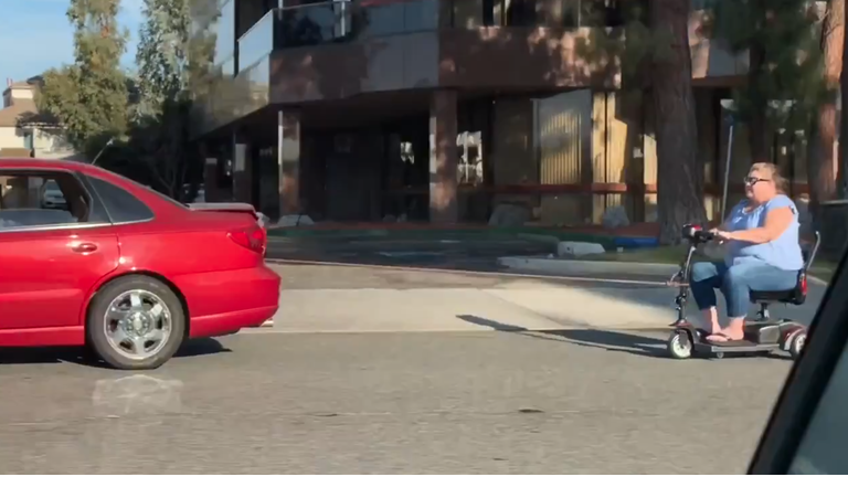 Woman on mobility scooter seen being towed by red sedan