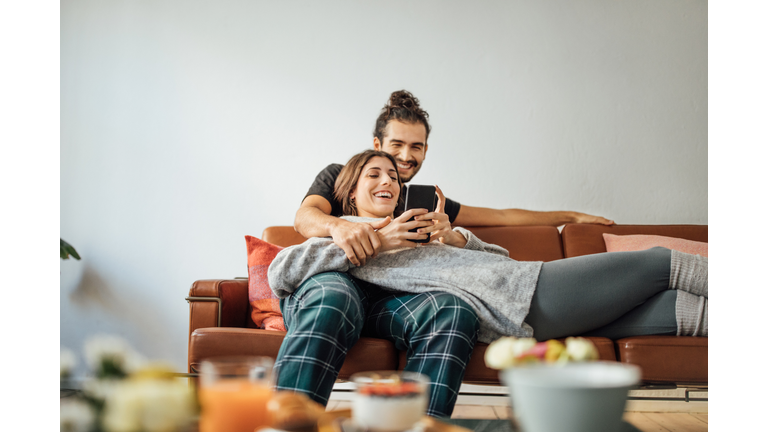 Young couple with smart phone relaxing on sofa