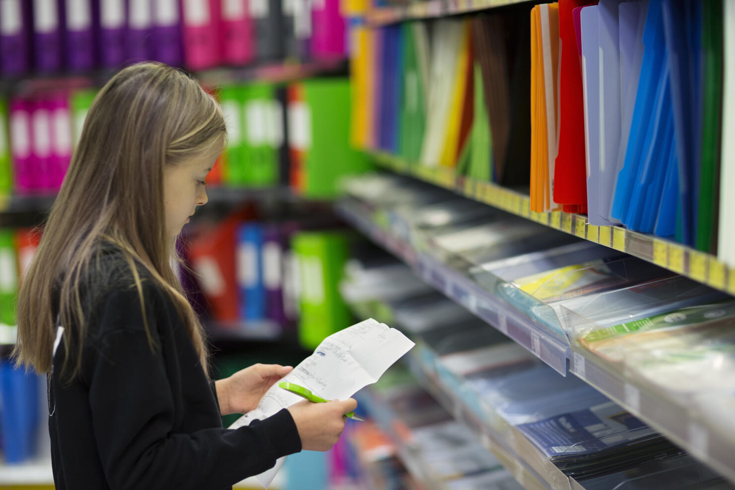 Girl (10-11) with shopping list looking for 'back to school' items in a store