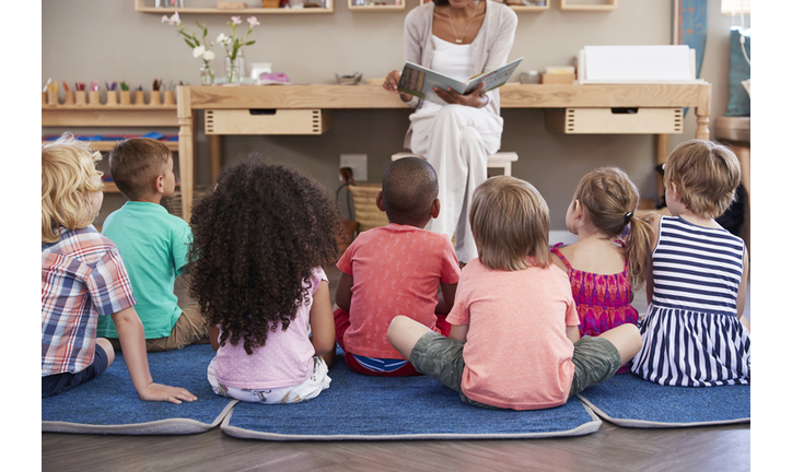 Teacher At Montessori School Reading To Children At Story Time