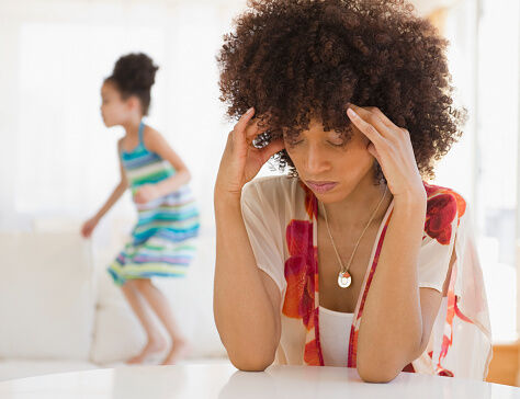 Mother with headache and daughter jumping on sofa