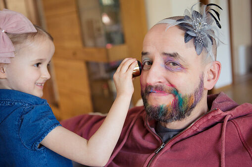 Girl (4-5) having fun putting makeup on her bemused father