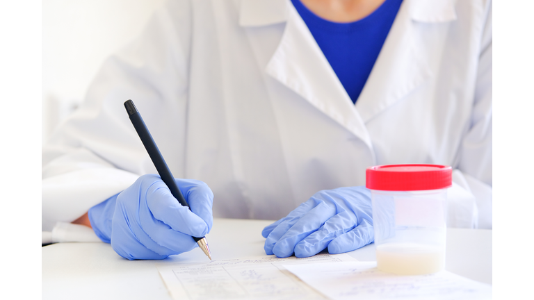 The doctor in medical gloves with a pen in his hands writes the results of studies or fills out forms documents. Next to the container with the semen analysis. Donor sperm for artificial insemination.