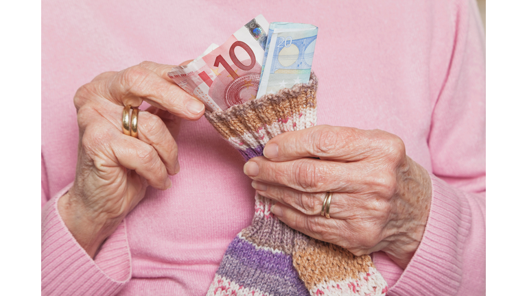 Germany, Senior woman counting money from money sock, mid section