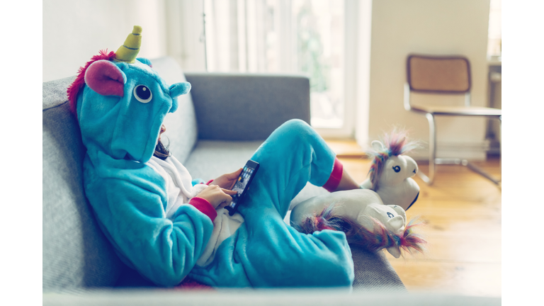 little girl in unicorn costume with mobile on couch