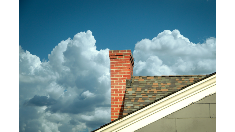 Part of tiled roof with brick chimney against clouds