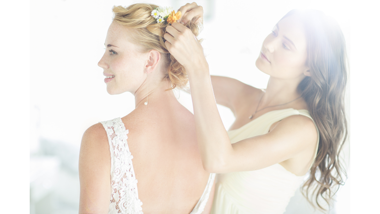 Bridesmaid helping bride with hairstyle in garden