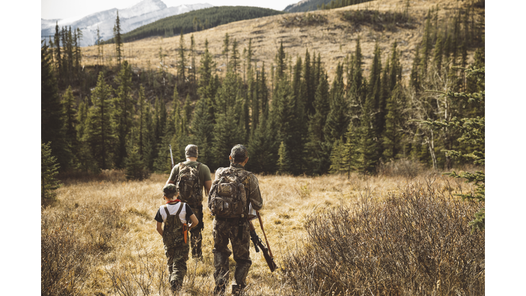 Multi-generation male hunters walking with hunting rifles in remote field