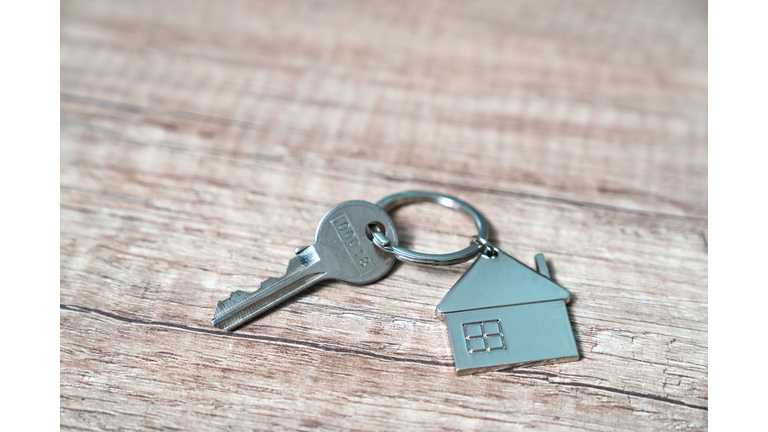 House key on a house shaped keychain resting on wooden floorboards concept for real estate, moving home or renting property